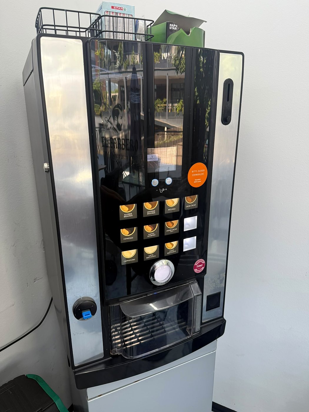 Kaffeeautomat in einem Barbershop, in voller Höhe auf einem Unterschrank: Wahlfeld mit Kleiner Brauner, Melange, Espresso und Latte Macchiato, darunter die Becherausgabe